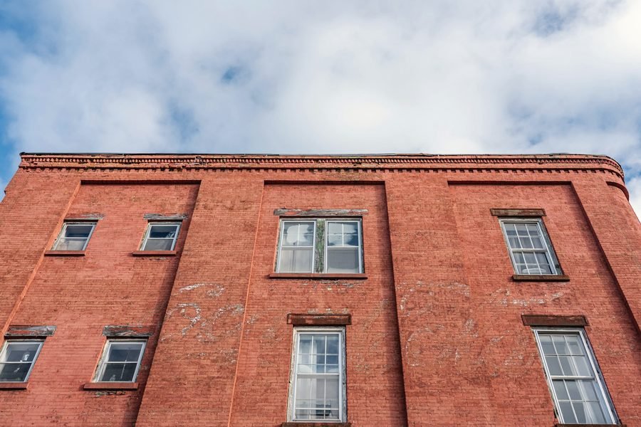 A three-storey red brick commercial building with white sash windows against a cloudy sky.