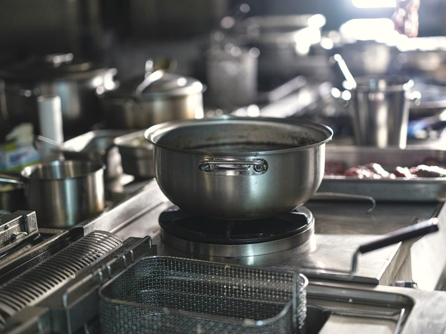 A steel pot on a range burner beside a fryer basket in a busy kitchen.
