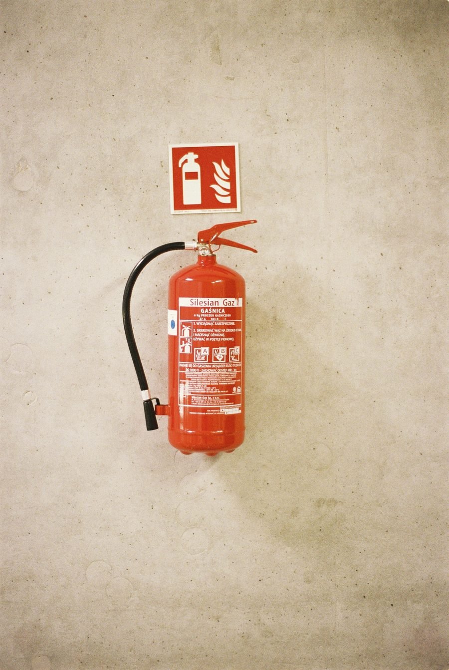 A small red extinguisher and sign on a pale plaster wall.