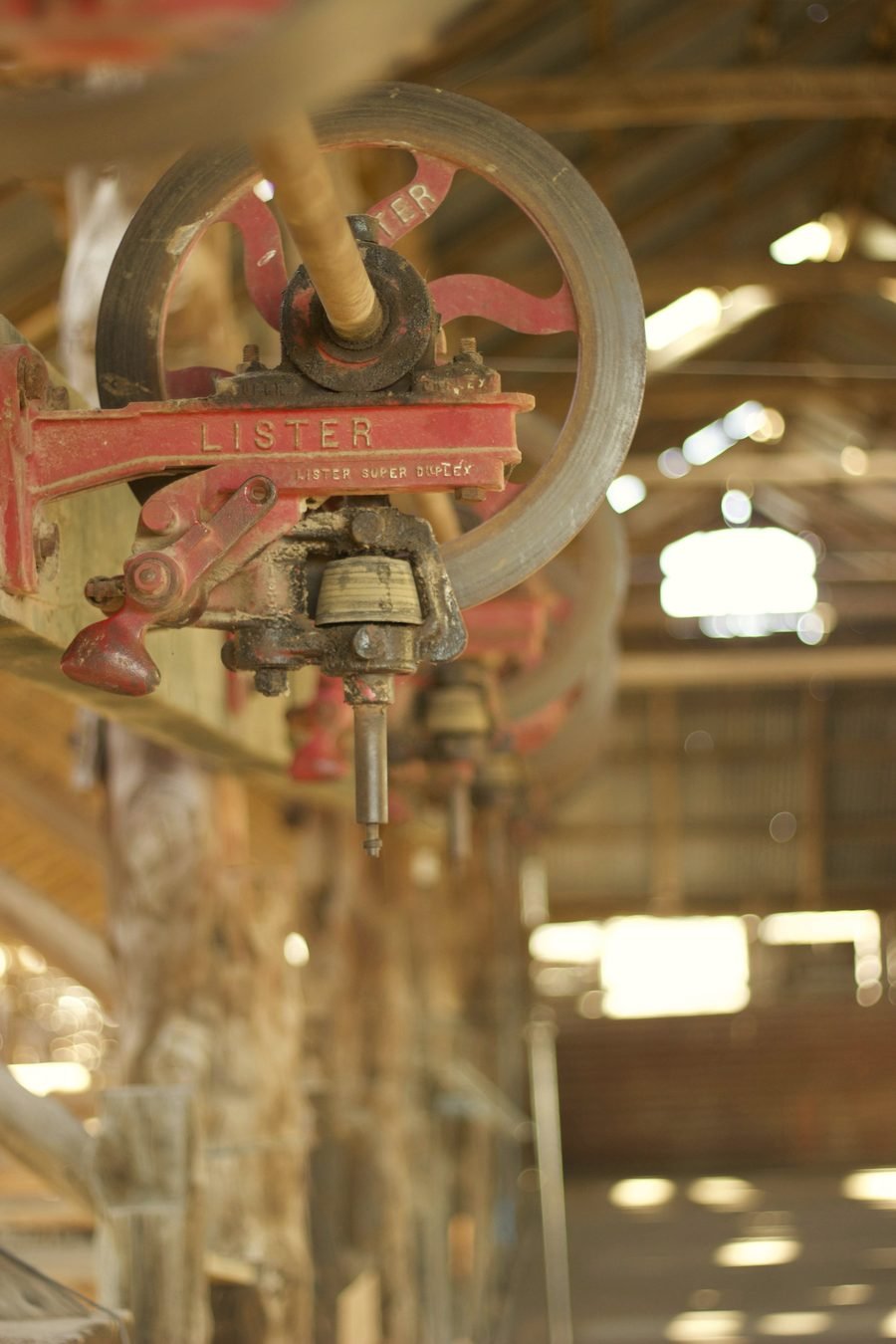 An old belt-driven drill press in a dusty workshop lit by high windows.