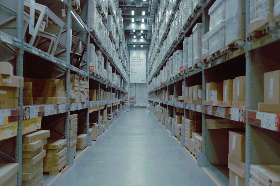 A long warehouse aisle between tall shelves of cardboard boxes.