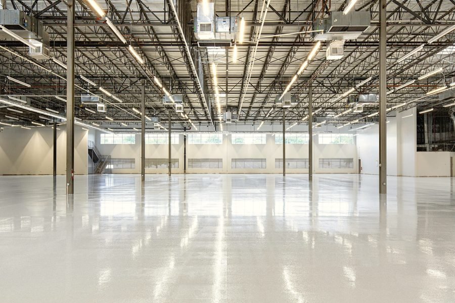 A wide empty warehouse with a polished concrete floor and steel roof trusses.